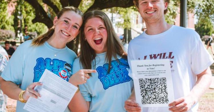 Three students registering others to vote posing for photo with registration documents