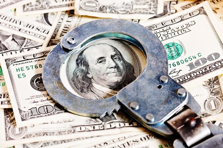 Handcuffs on top of 100 dollar bill and many 1 dollar bills 
