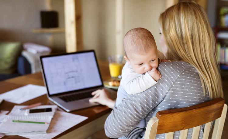 Mother holding baby while working on laptop