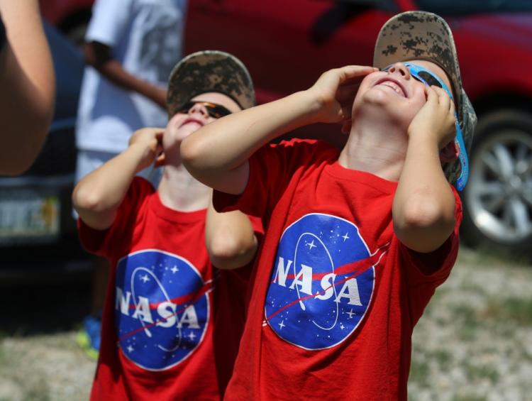 Two children with eclipse glasses, looking at sun, with NASA t-shirts