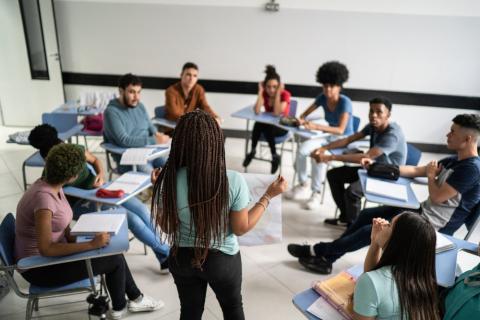 Person presenting in front of circle of students at their desks