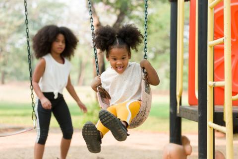 Child playing on swing with other child behind them, blurred in background