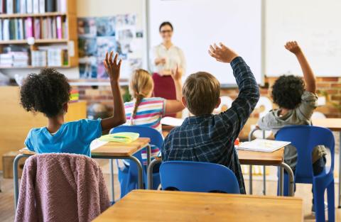 Seated children raising their hands in an elementary school clasroom