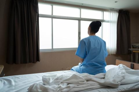Woman wearing a patient gown in her hospital room, on hospital bed, looking outside of window