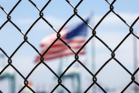 American flag blurred behind a metal wire fence