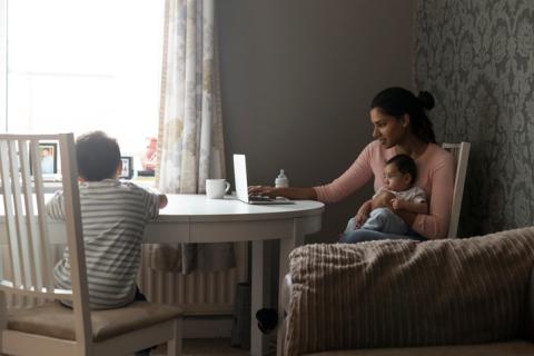 Mom working on laptop on kitchen table while taking care of two children 