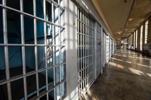 A row of prison cells with a long, grey corridor and windows 