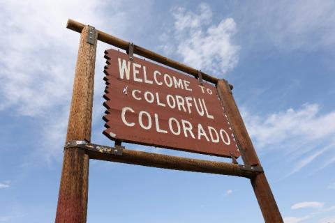 Brown road side made of wood with "Welcome to Colorful Colorado" written on it