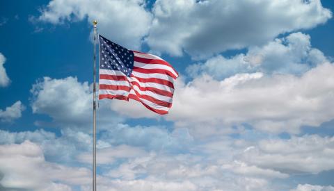 American flag on pole waving with blue, cloudy sky in background  