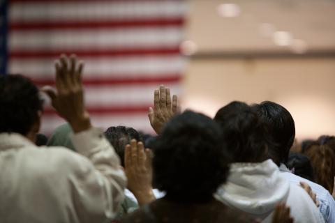 United States Citizenship Ceremony, people raising hands in front of U.S. flag 