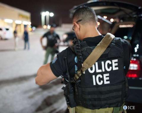 View of ICE agent from behind with black vest that reads "POLICE ICE"