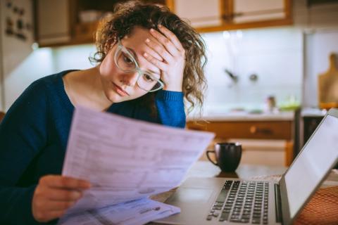 Woman with hand on forehead in front of laptop and bills, looking stressed 