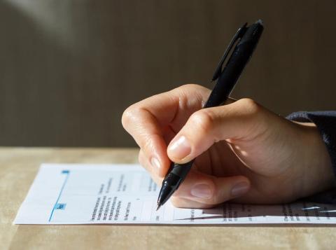 Checkbox: Hand holding a pen filling out a form