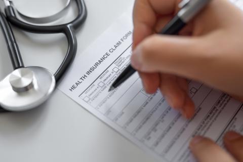 Person's hand filling out health insurance claim form 