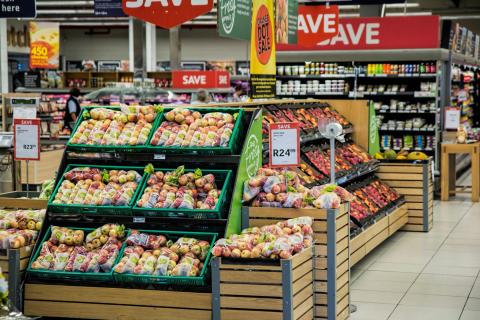 Grocery store produce section with bagged apples on display and sale signs overhead.