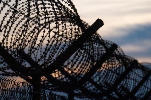 barbed wire on top of fence at a detention facility with sun setting in the background 