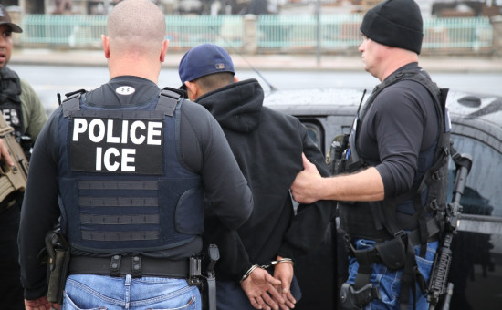 Two ICE officers arresting an individual, whose hands are handcuffed behind their back