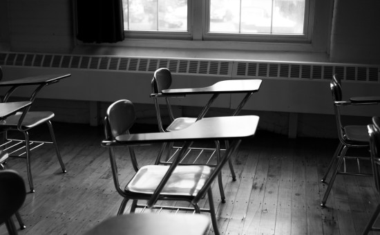 Black and white image of an empty desk in a high school classroom
