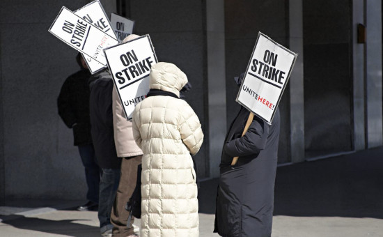 Hotel workers on strike outside of workplace carrying signs with "On Strike"