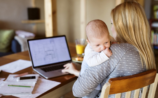 Mother holding baby while working on laptop