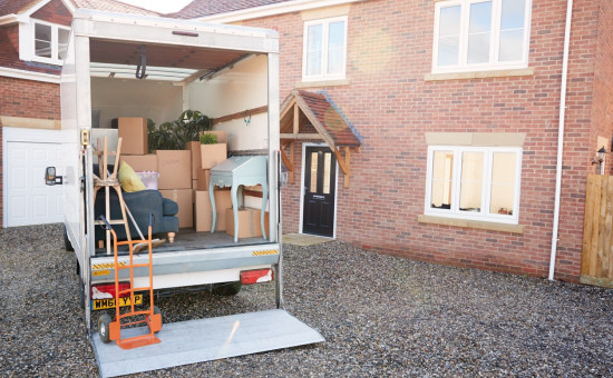 Moving truck filled with boxes and furniture, parked next to a brick building