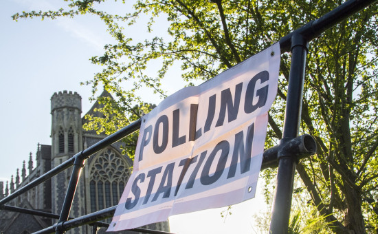 White sign with black lettering attached to railing that reads "POLLING STATION"