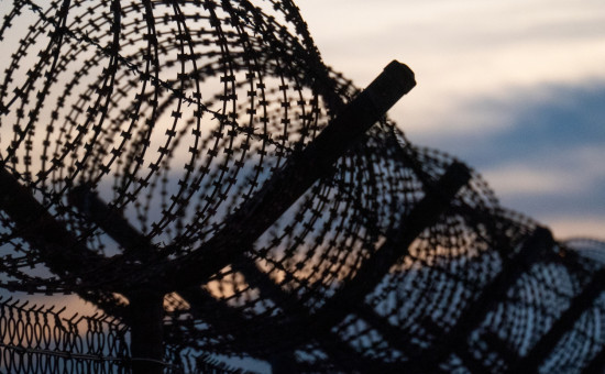 barbed wire on top of fence at a detention facility with sun setting in the background 